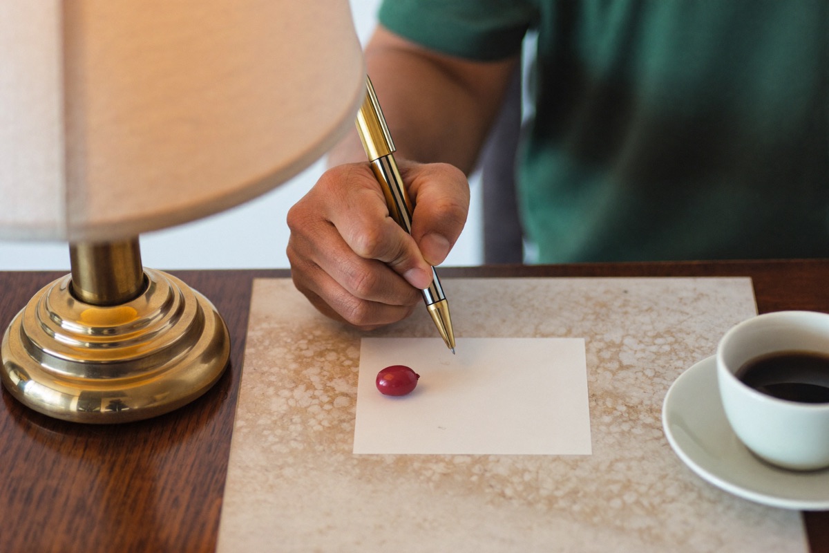 A hand holding a pen above a small blank card on a counter under a lamp