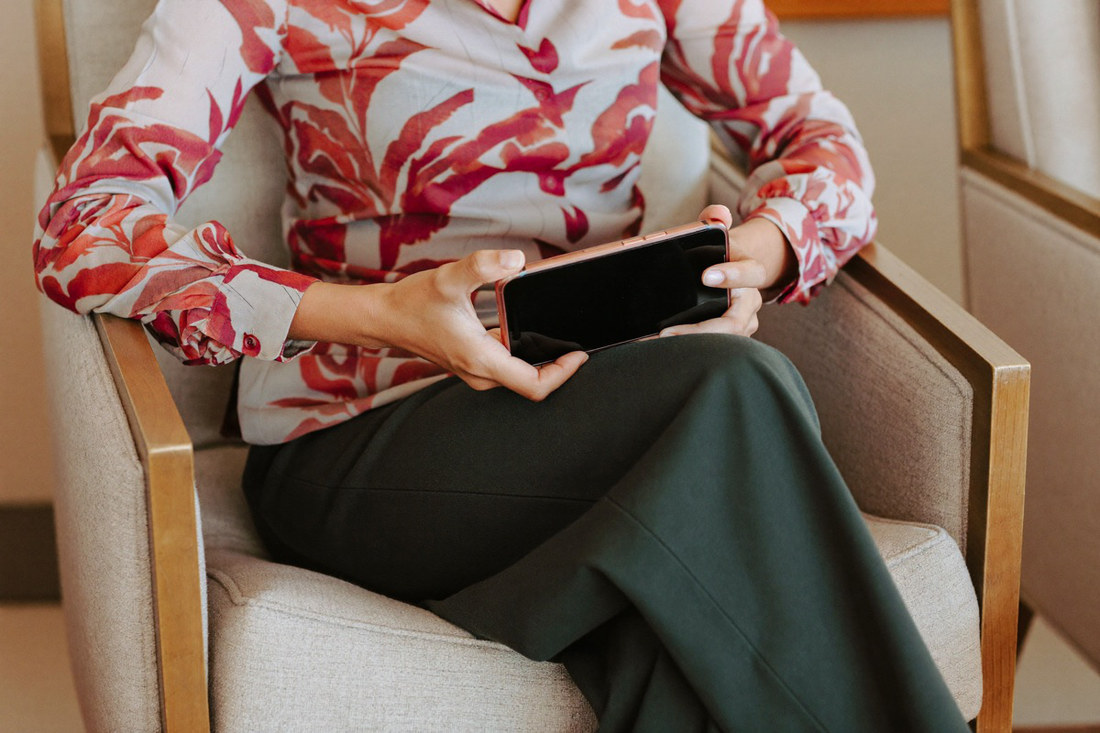 A woman in a hotel lounge armchair holding a large phone with a dark screen