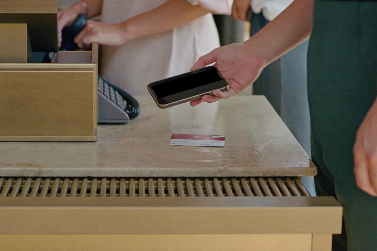 A hand holding a dark phone above a cashier counter beside a bank card