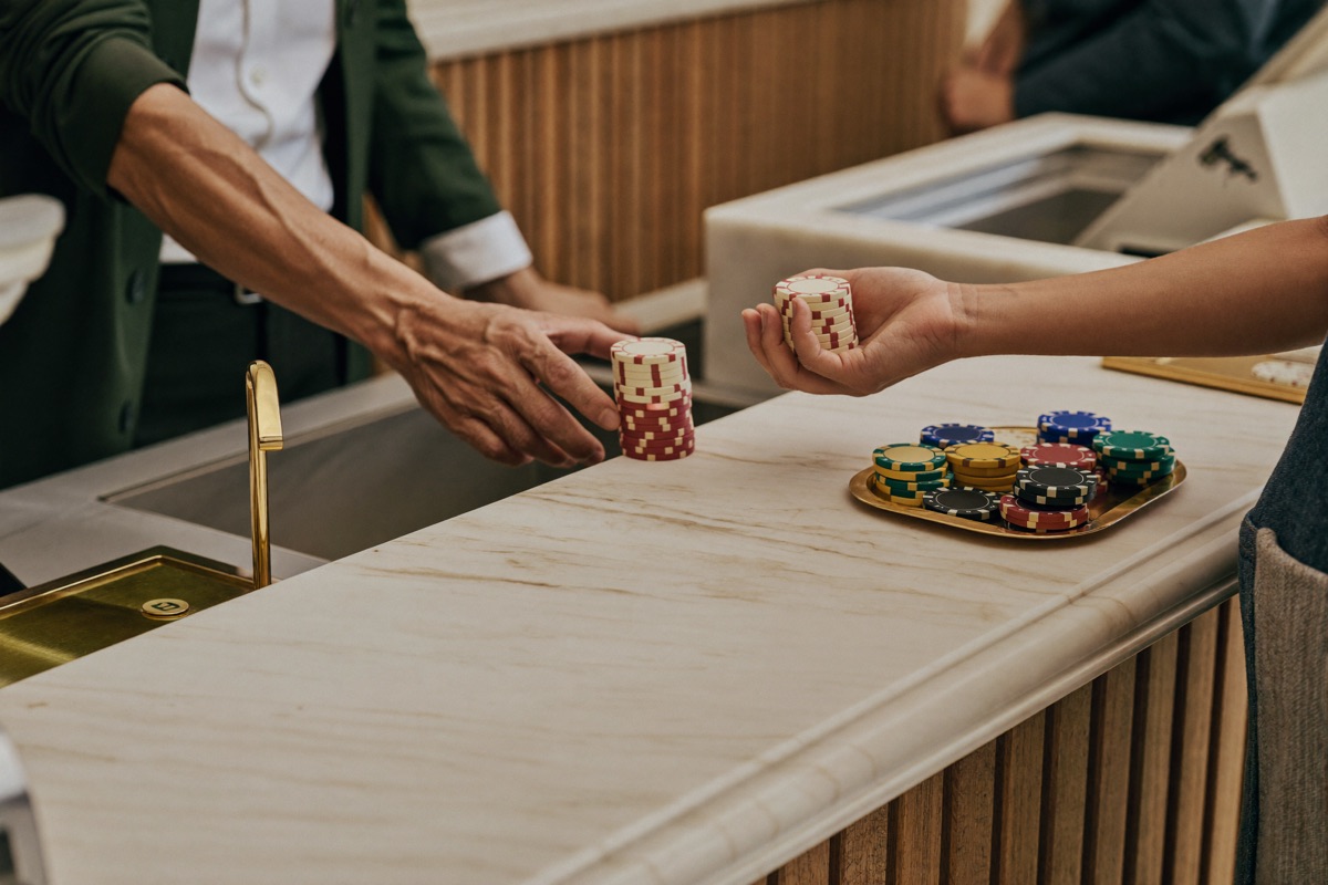A cashier counting ringgit banknotes onto a counter beside a tray of chips