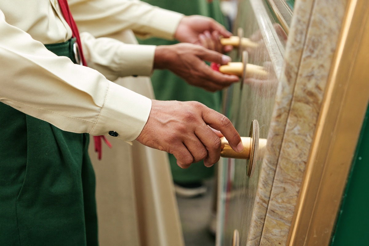 A hand resting on the spin button of a slot cabinet, the reel glass lit behind